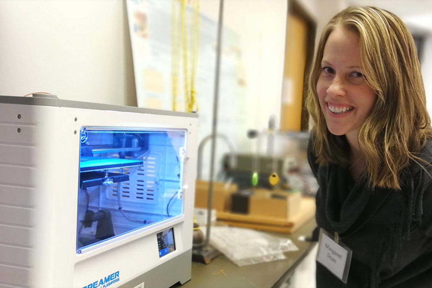 A woman smililng next to a 3D printer