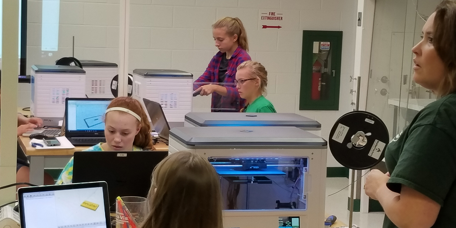 Middle school girls and their teacher in a computer lab using 3D printers