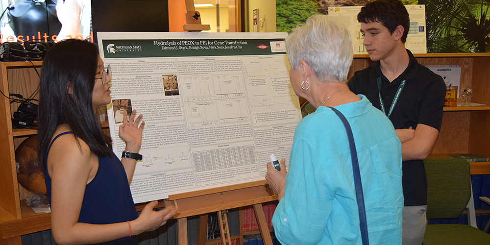 Students present research poster to guest during reception