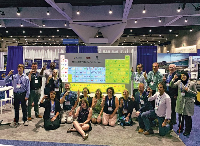 Group of people from the Chemists with Disabilities committee in front of periodic table display with each person doing sign language