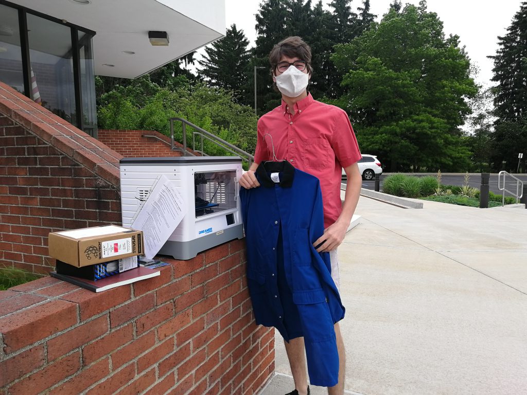 Young man holding a lab coat standing outside.